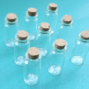 May include: Ten small glass bottles with cork stoppers. The bottles are clear and the corks are brown. The bottles are arranged in a circle on a blue surface.