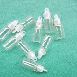 May include: Eight clear glass bottles with white dropper tops and a small loop on the top. The bottles are arranged in a star shape on a green surface.