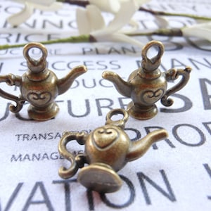 May include: Three antique gold-toned teapot charms with heart details. The charms are on a white background with printed text.