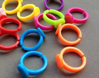 May include: A collection of colorful plastic rings with a flat, round top. The rings are in various colors, including red, orange, yellow, green, blue, purple, and pink.