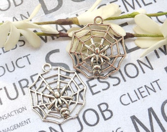May include: Two silver charm pendants shaped like spiderwebs with a spider in the centre. The spiderwebs are detailed and intricate.