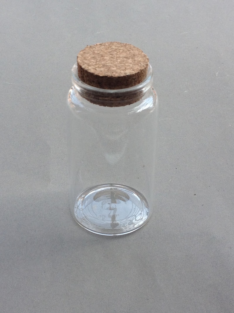 May include: A clear glass bottle with a cork stopper. The bottle is empty and has a textured surface.