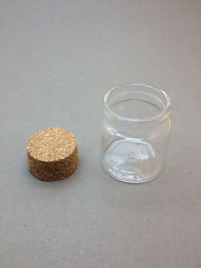 May include: A clear glass jar with a cork lid. The jar is empty and has a round shape.