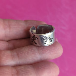 May include: A silver ring with a dragonfly design. The ring is open and adjustable.