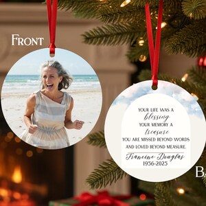 May include: A round, white Christmas ornament with a red ribbon. The front features a photo of a woman on a beach. The back has text that reads "Your life was a blessing, your memory a treasure... Francine Douglas 1956-2025."