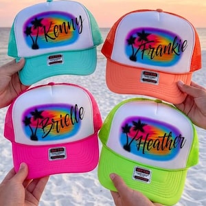 May include: Four trucker hats with white front panels featuring a rainbow airbrushed sunset and palm tree graphic. The hats are personalized with the names Kenny, Frankie, Brielle, and Heather in black script. Each hat has a unique neon brim and mesh.