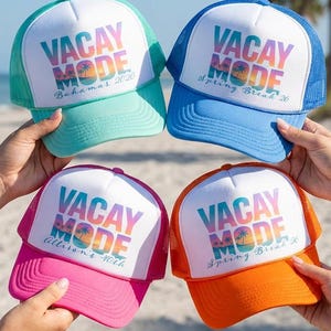 May include: Four colorful trucker hats with the words "VACAY MODE" printed on the front. The hats are in shades of teal, blue, pink, and orange. Each hat has a white front panel with a different vacation destination and year.