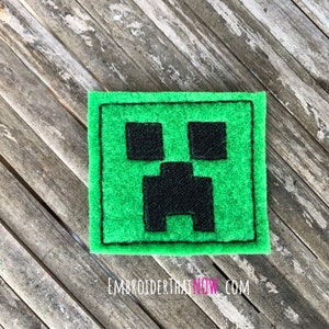 Op de afbeelding: Een groene viltpatch met een zwart geborduurd Minecraft Creeper-gezicht.