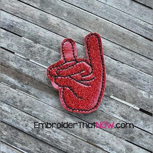 May include: A red foam hand in the shape of a peace sign, with a glittery texture and black stitching around the edges. The foam hand is on a weathered wooden surface. The text "Embroider ThatNOW.com" is visible.