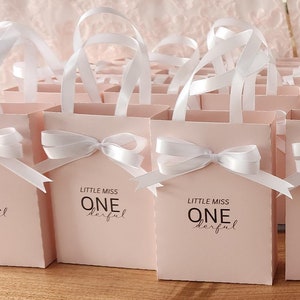 May include: Pink favor bags with white ribbon bows and the text "Little Miss One Derful" printed on the front.