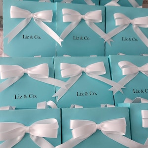 May include: A group of 12 turquoise blue gift boxes with white satin ribbon bows and the text "Liz & Co." printed on the front of each box.