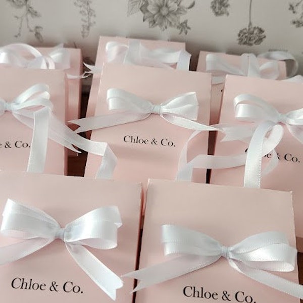 Sacolas de lembrancinhas. Sacolas pequenas e elegantes em tom rosa claro/rosa claro com alças de fita de cetim e nome personalizado.