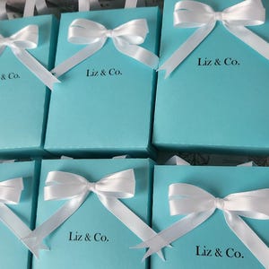 May include: Six turquoise blue gift boxes with white satin ribbon bows and the text "Liz & Co." printed on the front of each box.