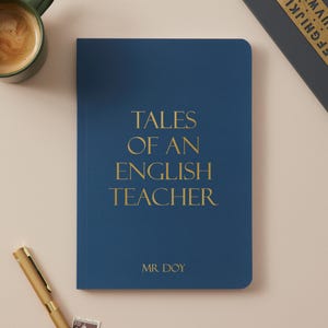 May include: A dark blue notebook with gold text reading "TALES OF AN ENGLISH TEACHER" and "MR. DOY". A gold pen, a green mug with coffee, and a small stamp are also visible.