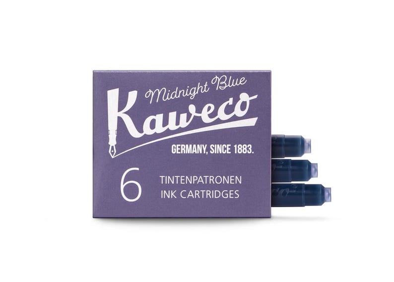 Pu&ograve; includere: Una scatola di cartucce d'inchiostro Kaweco Midnight Blue. La scatola &egrave; di colore viola scuro con testo bianco che recita "Midnight Blue Kaweco GERMANY, SINCE 1883. 6 TINTENPATRONEN INK CARTRIDGES". Sono visibili tre cartucce d'inchiostro blu.