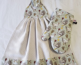 May include: A kitchen set featuring a hanging towel and oven mitt. Both items have a light green background with a repeating pattern of roosters, wheat, and eggs. The towel has a waffle weave texture and a decorative border with the rooster pattern.
