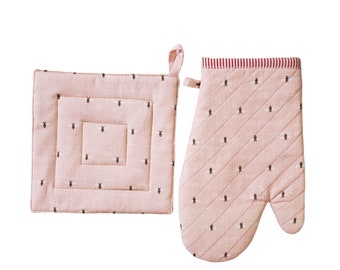 May include: A pink quilted oven mitt and matching square pot holder set. The set features a small black bee pattern on a dotted background. The top of the oven mitt has a red and white striped trim, and both pieces have a loop for hanging.