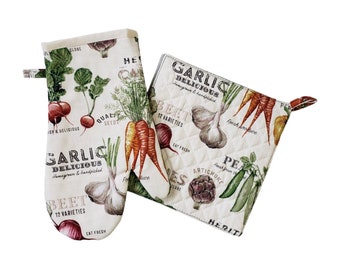 May include: A cream-colored oven mitt and pot holder set featuring a vegetable print. The design includes illustrations of carrots, garlic, beets, and peas, with text that reads "GARLIC DELICIOUS" and "BEET 12 VARIETIES".
