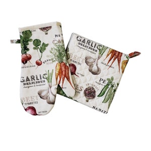 May include: A cream-coloured oven mitt and pot holder set with a vegetable print. The design features illustrations of carrots, garlic, beets, and peas, with text that reads "GARLIC DELICIOUS" and "BEET 12 VARIETIES".