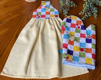 May include: A yellow kitchen towel and oven mitt set. The towel has a checkered top with fruit and vegetable designs. The oven mitt has a matching checkered pattern with a blue trim. The set is designed for kitchen use.