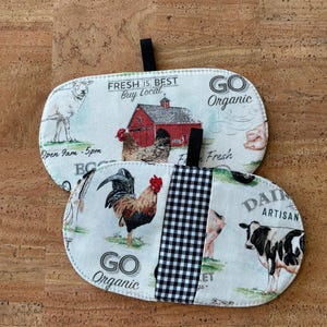 May include: Two oval fabric pot holders with black hanging loops. One shows a farm scene with a red barn, chickens, and the text "FRESH IS BEST Buy Local." The other has a rooster, cow, pig, and the text "GO Organic."