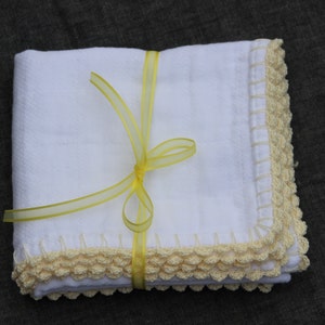May include: A stack of white, square cloths with a crocheted cream border. The cloths are tied with a yellow ribbon. The background is a dark, plain colour.