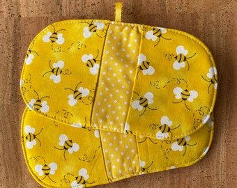 May include: Yellow oven mitt with a bee pattern. The mitt features a repeating pattern of black and yellow bees with white wings on a yellow background. A white polka dot pattern is on the center panel. A small yellow loop is attached for hanging.