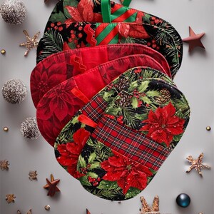 May include: A collection of Christmas stockings featuring festive designs such as poinsettias, tartan, and foliage. The stockings are in red, black, and green, with green ribbon loops. The scene is decorated with stars and ornaments.