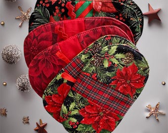 May include: A stack of Christmas stockings with various patterns, including poinsettias, plaid, and greenery. The stockings are red, black, and green, with green ribbon loops. Decorative stars and ornaments surround the stockings.