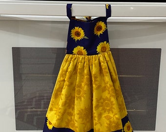 May include: A yellow and navy blue kitchen towel with a sunflower design. The towel is hanging on a white oven. The top portion of the towel is navy blue with yellow sunflowers. The bottom portion is yellow with a sunflower pattern.