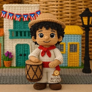 Pode incluir: Boneca de crochê de um músico usando chapéu, cachecol vermelho e roupa branca, segurando um tambor. A boneca está em frente a edifícios de crochê com bandeiras de Porto Rico. O texto "BOTONES VALIENTES" é visível.