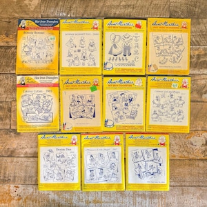 May include: Eleven yellow and white paper packets of Aunt Martha's hot iron transfers featuring various line art illustrations of children, animals, and alphabets. Each packet displays a unique title, design number, and black ink drawings.