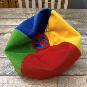 May include: A multi-coloured beanbag chair in blue, green, yellow, and red sections. A red patch with a blue paw print design is centered on the beanbag. The beanbag is designed for children.
