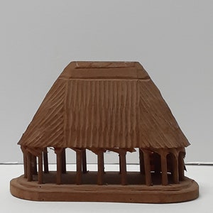 以下が含まれることがあります： 屋根と柱のある建物の小さな茶色の粘土模型。模型は粗い質感の粘土でできています。
