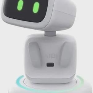 May include: A white AI robot with a rounded head and body, featuring a black screen with two green oval eyes. The robot sits on a circular base with a glowing blue and green light. The word "AIBI" is printed on the body.