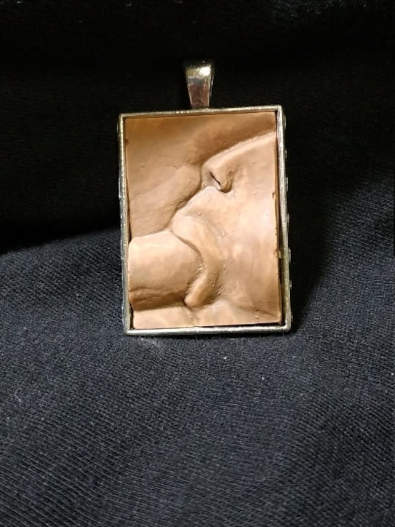 May include: A silver pendant with a rectangular brown clay cameo depicting a sculpted image of a face and lips.