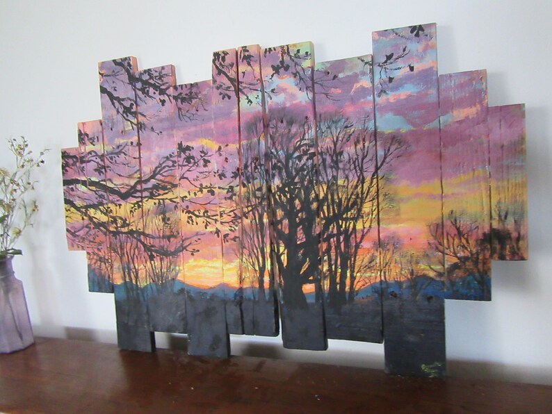 May include: A sunset scene painted on wooden planks, with a silhouette of trees in the foreground and a colorful sky in the background.