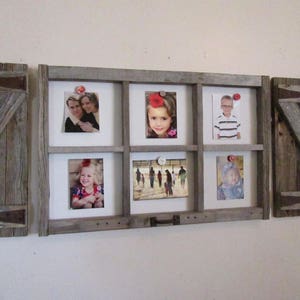 May include: A rustic wooden picture frame with six photo openings, flanked by two wooden shutters. The frame holds various photos, secured with decorative pins. The wood has a weathered, gray appearance, adding a vintage aesthetic.