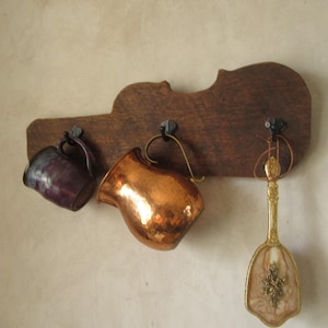 Könnte beinhalten: Ein wandmontierter Holzständer in Form einer Geige mit drei Haken. An den Haken hängen ein Kupferkrug, eine lila Tasse und ein goldfarbener Dekorationslöffel.