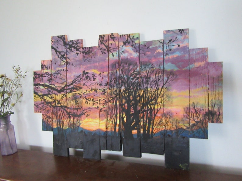 May include: A sunset scene painted on wooden planks. The painting features a silhouette of trees against a colorful sky with shades of pink, purple, orange, and yellow. The planks are arranged in a staggered pattern to create a unique and rustic look.