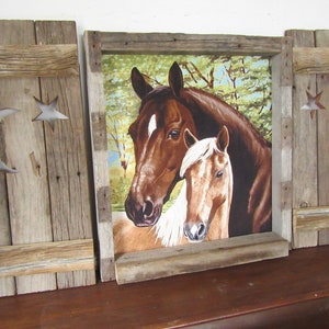 May include: A rustic wooden frame with two shutters on either side, featuring a cutout of a crescent moon and star. The frame holds a printed image of two horses, one brown and one light brown, in a forest setting.