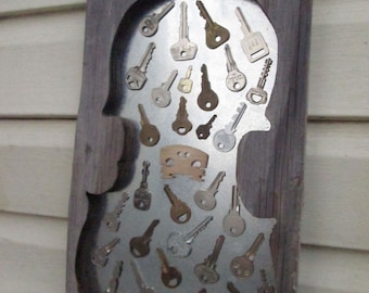 May include: A wooden frame with a metal cutout of a violin. The cutout is filled with a variety of old keys.