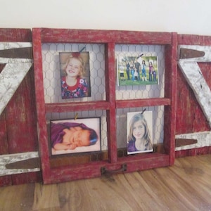 May include: A red wooden picture frame with a chicken wire backing. The frame is divided into four sections, each holding a photo. The photos are of a young girl, a baby, a family, and a young woman.