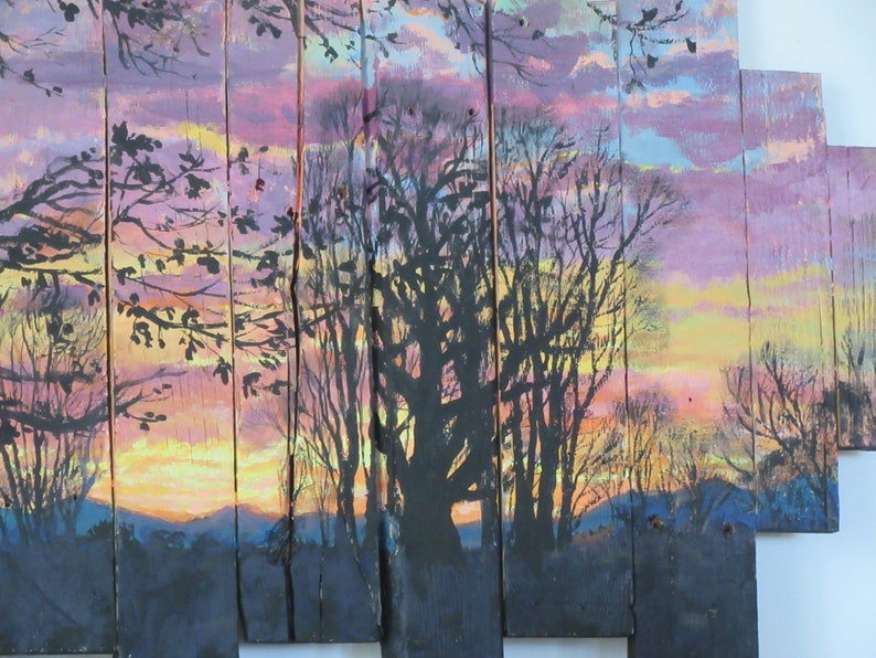 May include: A painting on wooden panels depicting a sunset scene with silhouetted trees. The sky is painted in shades of pink, purple, and yellow, with a hint of orange at the horizon. The trees are black and appear to be in a forest setting.