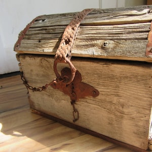 Puede incluir: Un cofre de madera rústico con una correa de cuero y herrajes metálicos. El cofre está hecho de madera desgastada y tiene un aspecto desgastado y antiguo.