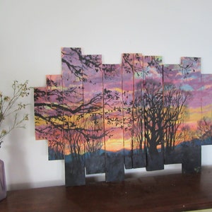 May include: A sunset scene painted on wooden planks, with a silhouette of trees and a colorful sky. The planks are arranged in a staggered pattern to create a unique and modern look.