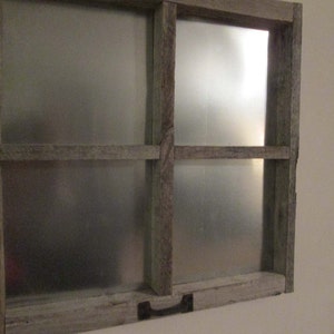 May include: A rustic, wooden framed wall decor piece with a metal insert. The frame is made of weathered, light-colored wood, and the metal insert has a silver finish. A small, dark-colored handle is attached to the bottom.