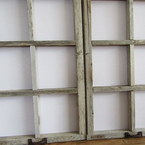 May include: Two rustic, weathered wooden window frames with eight panes each. The frames are a muted gray color, and the panes are filled with a white material. Each frame has a small, dark metal handle.