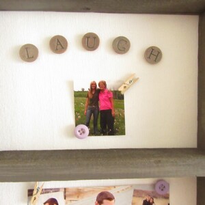 May include: A gray wooden framed display with the word "LAUGH" spelled out with circular wooden letters. A photo is attached with a clothespin and a purple button. Additional photos are visible below.