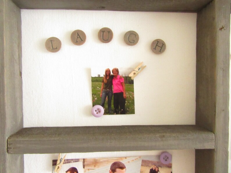 May include: A gray wooden framed display with the word "LAUGH" spelled out with circular wooden letters. A photo is attached with a clothespin and a purple button. Additional photos are visible below.